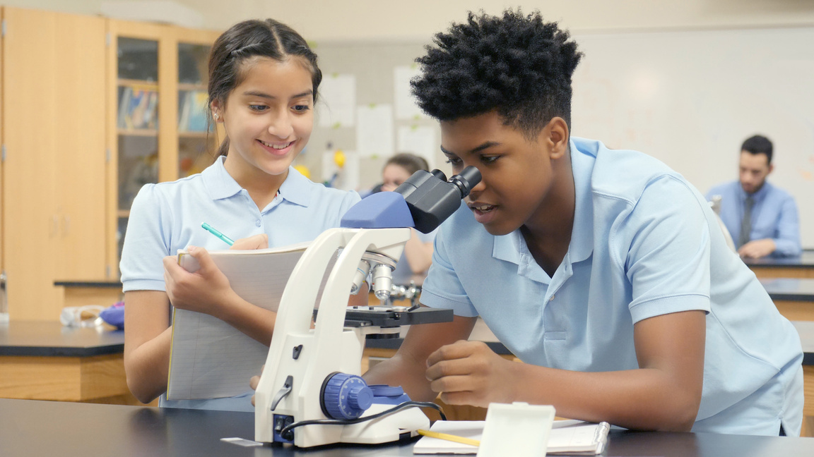 Teen boy uses microscope in school science class